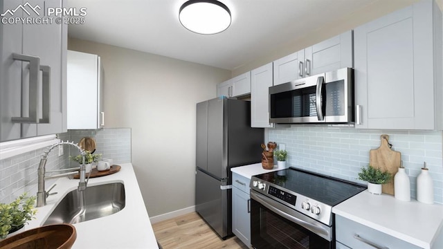 kitchen featuring a sink, light wood-style floors, light countertops, appliances with stainless steel finishes, and tasteful backsplash