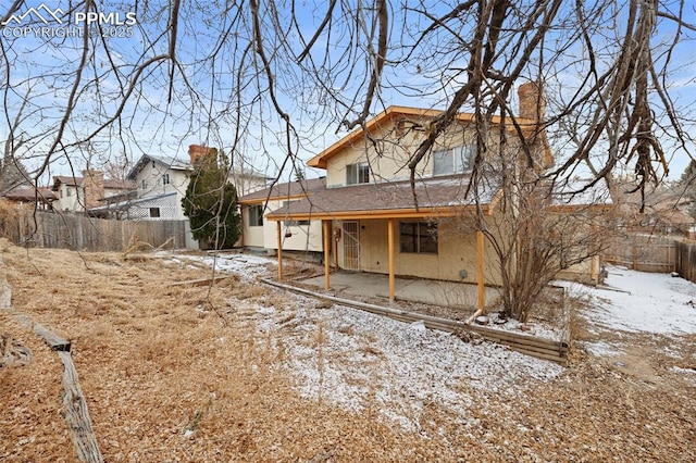 snow covered property with a patio area, a fenced backyard, and a chimney