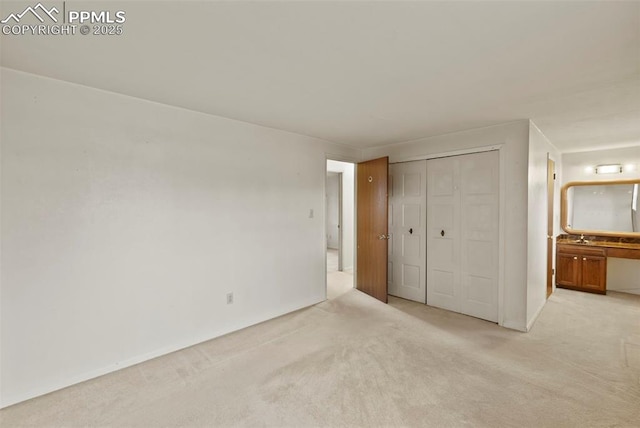 unfurnished bedroom with light carpet, a closet, a sink, and ensuite bathroom