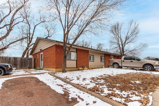 snow covered property with brick siding and fence