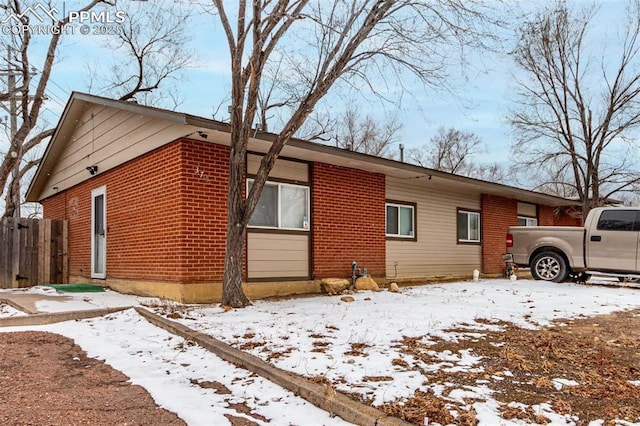 view of snowy exterior with brick siding and fence