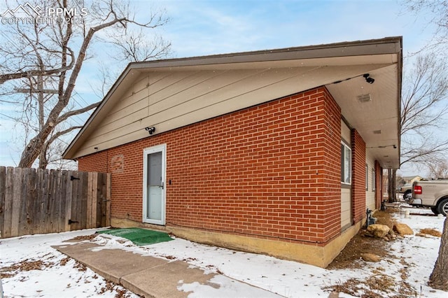 view of snowy exterior with brick siding and fence