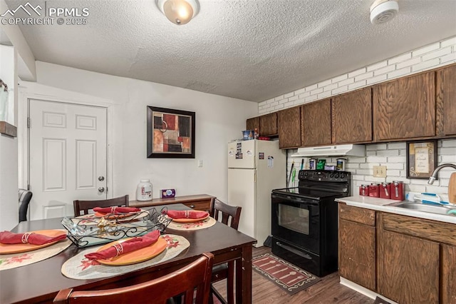 kitchen featuring dark wood-style flooring, black range with electric stovetop, freestanding refrigerator, under cabinet range hood, and a sink