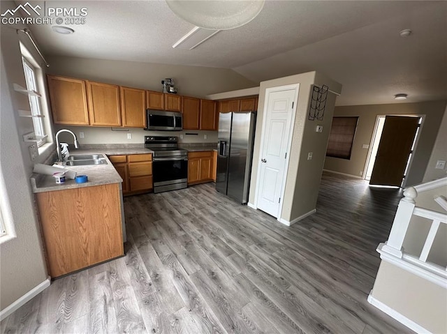 kitchen featuring brown cabinetry, vaulted ceiling, stainless steel appliances, light countertops, and a sink