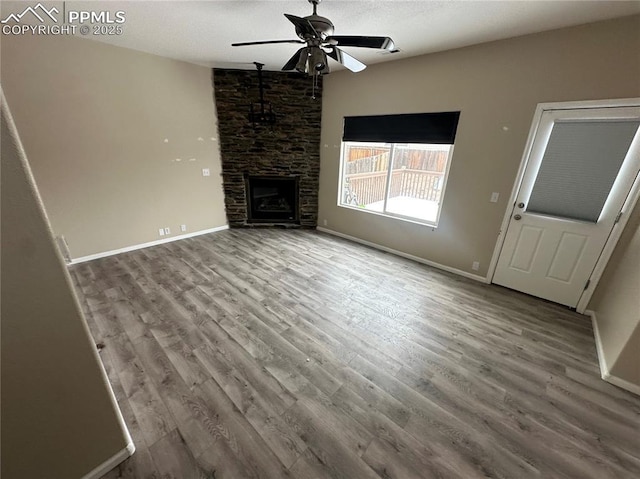 unfurnished living room featuring ceiling fan, a stone fireplace, baseboards, and wood finished floors