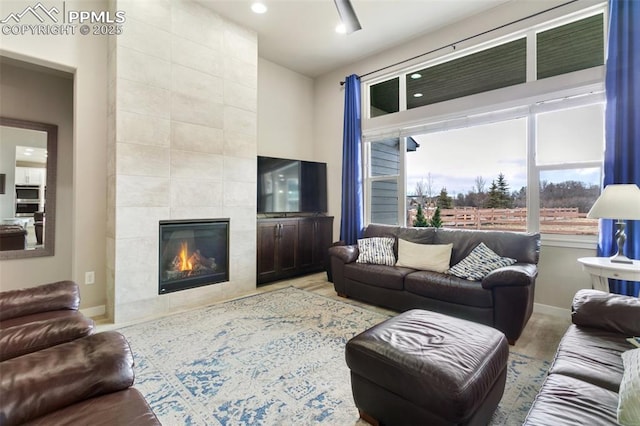 living area featuring baseboards, a tiled fireplace, and wood finished floors