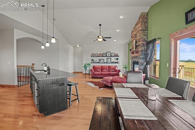 dining room with high vaulted ceiling, a stone fireplace, recessed lighting, a ceiling fan, and light wood-type flooring