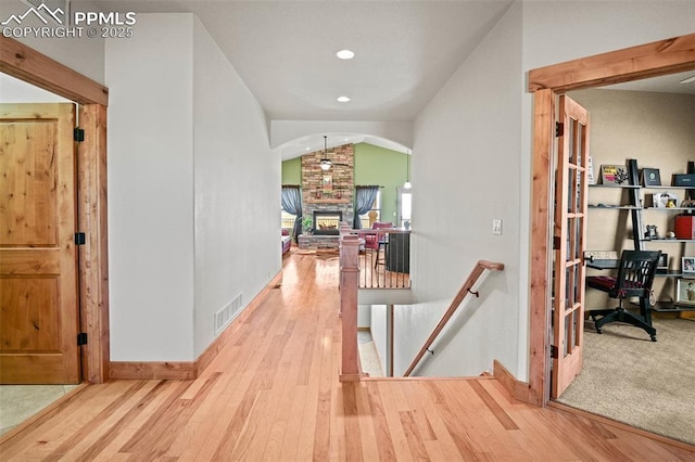 hallway with lofted ceiling, wood-type flooring, an upstairs landing, and visible vents