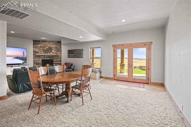 carpeted dining room with french doors, visible vents, a stone fireplace, and baseboards