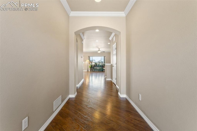 corridor featuring visible vents, dark wood-type flooring, ornamental molding, arched walkways, and baseboards