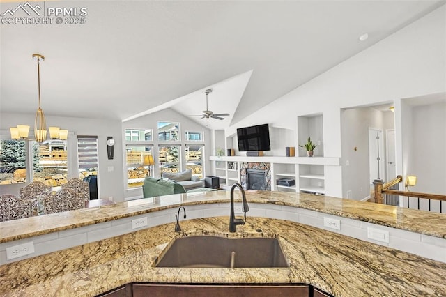 kitchen with lofted ceiling, light stone counters, a sink, and a glass covered fireplace