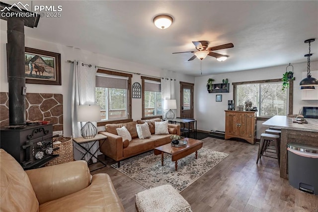 living area featuring a wood stove, a ceiling fan, dark wood finished floors, and a wealth of natural light