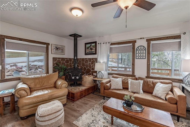 living room featuring wood finished floors, a wood stove, and a ceiling fan