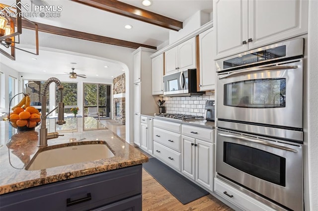 kitchen with white cabinetry, stainless steel appliances, a sink, and dark stone counters