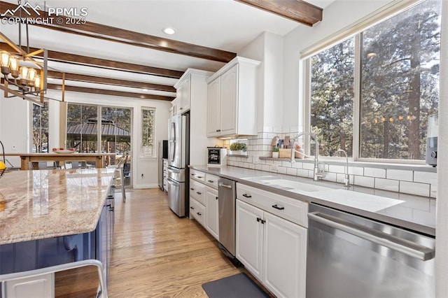 kitchen featuring stainless steel appliances, pendant lighting, white cabinetry, and light stone countertops