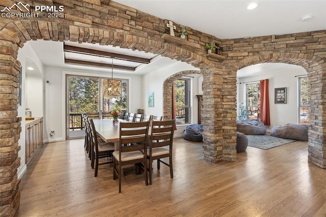 dining area featuring a healthy amount of sunlight, light wood-style flooring, arched walkways, and a raised ceiling