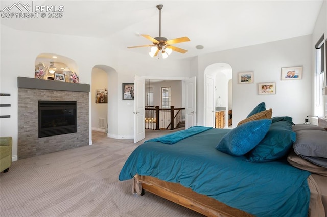 bedroom featuring baseboards, visible vents, a glass covered fireplace, light colored carpet, and ensuite bathroom