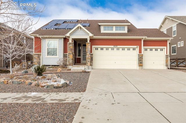 view of front of house featuring stone siding, concrete driveway, an attached garage, and solar panels