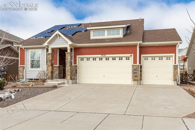 view of front facade featuring roof with shingles, roof mounted solar panels, a garage, stone siding, and driveway