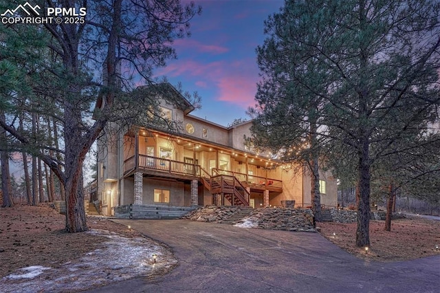 view of front of house with driveway, stone siding, stairway, and stucco siding