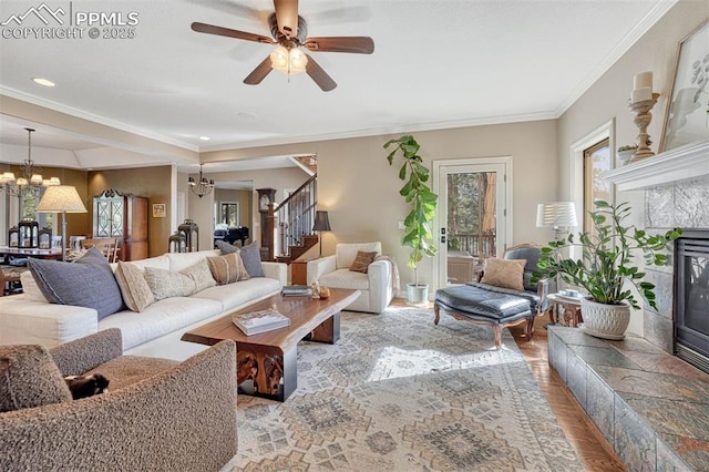 living room featuring crown molding, stairway, a premium fireplace, wood finished floors, and ceiling fan with notable chandelier