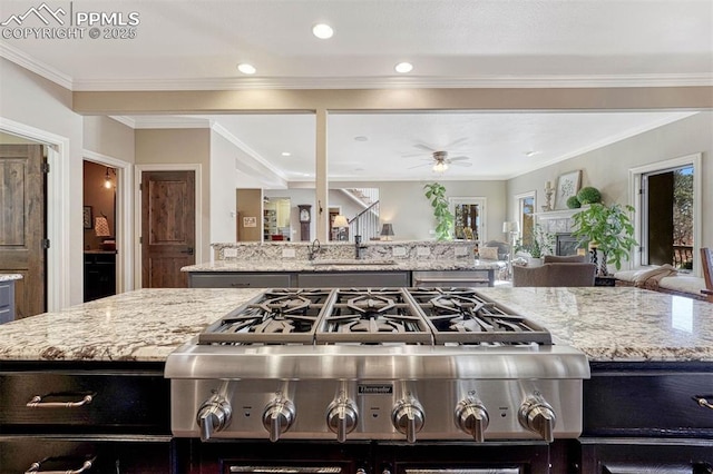 kitchen featuring ceiling fan, light stone counters, stove, open floor plan, and crown molding