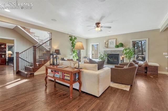 living room featuring dark wood-style floors, crown molding, stairway, a tile fireplace, and baseboards