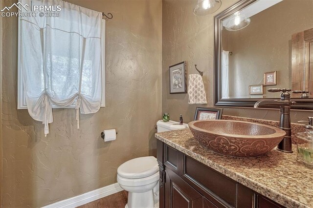 bathroom featuring a textured wall, vanity, toilet, and baseboards