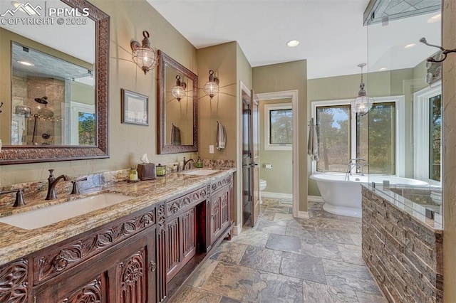 full bathroom featuring a freestanding bath, a sink, stone tile flooring, and baseboards