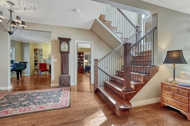 stairway with a notable chandelier, baseboards, wood finished floors, and ornamental molding