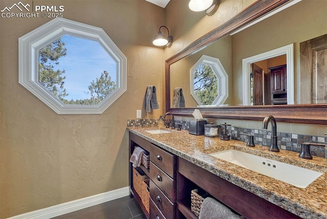 bathroom featuring a textured wall, a sink, and baseboards