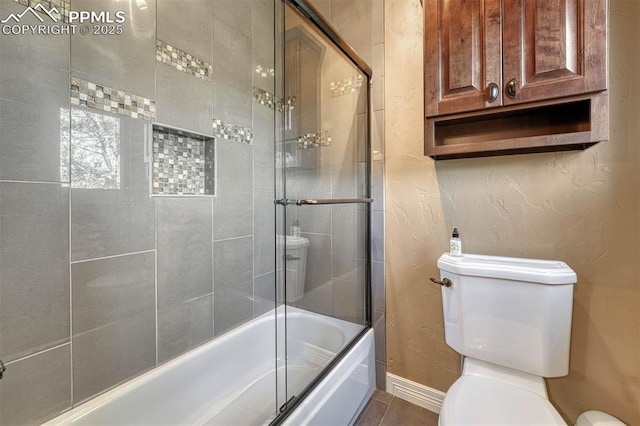 full bath with baseboards, a textured wall, toilet, shower / bath combination with glass door, and tile patterned floors