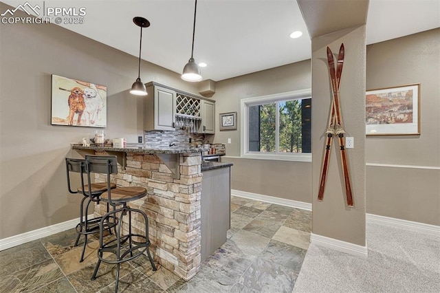 bar featuring indoor bar, tasteful backsplash, hanging light fixtures, stone finish flooring, and baseboards