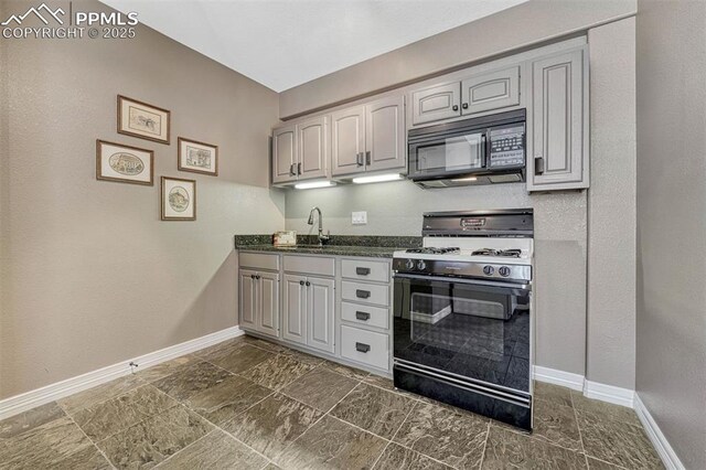 kitchen featuring black appliances, dark countertops, a sink, and baseboards