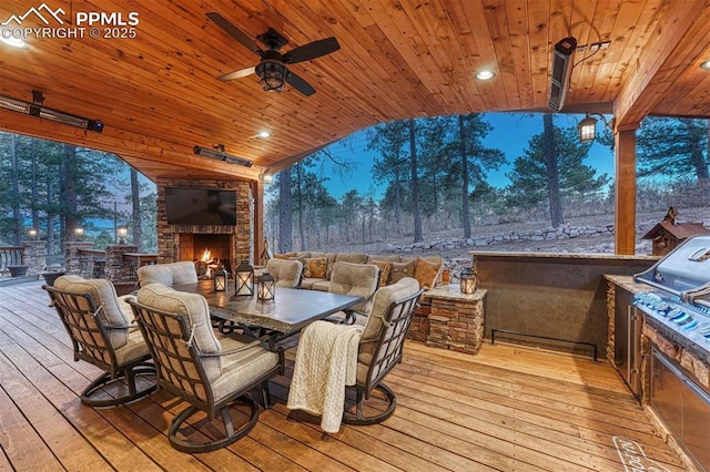 deck with outdoor dining space, an outdoor stone fireplace, exterior kitchen, and a ceiling fan