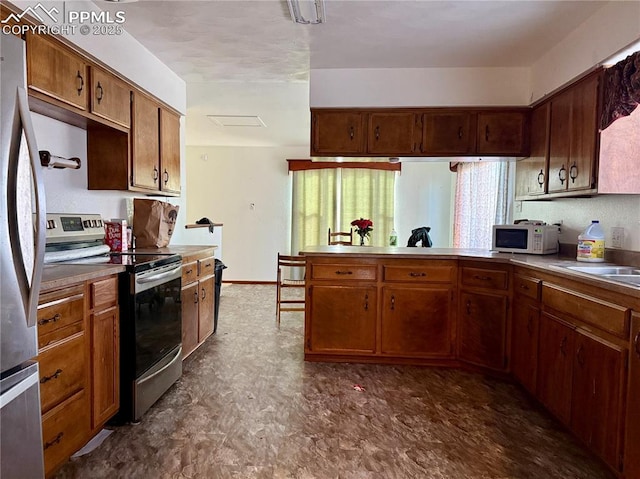 kitchen featuring dark floors, stainless steel appliances, brown cabinetry, a sink, and a peninsula