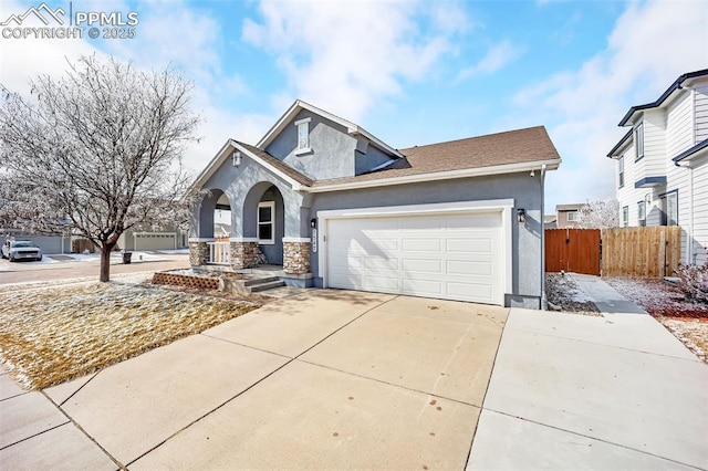 view of front of home with driveway, stone siding, an attached garage, fence, and stucco siding