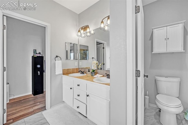 full bathroom with toilet, marble finish floor, double vanity, and a sink