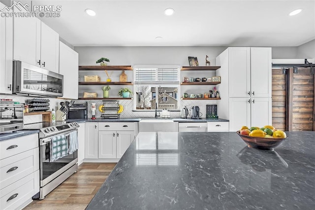 kitchen featuring stainless steel appliances, a sink, white cabinets, dark stone counters, and open shelves