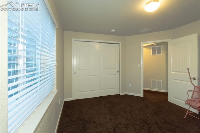 unfurnished bedroom featuring a closet, dark carpet, visible vents, and baseboards