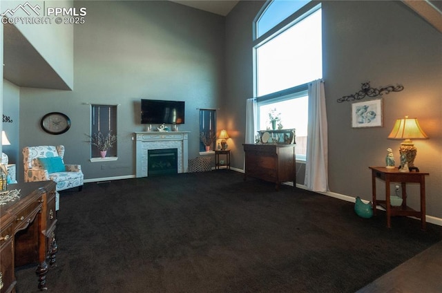 living room featuring dark carpet, baseboards, a fireplace, and a high ceiling