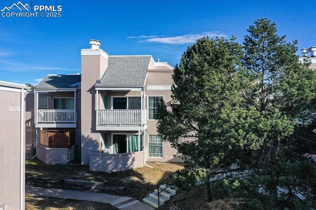 exterior space featuring a balcony, stucco siding, a chimney, and roof with shingles