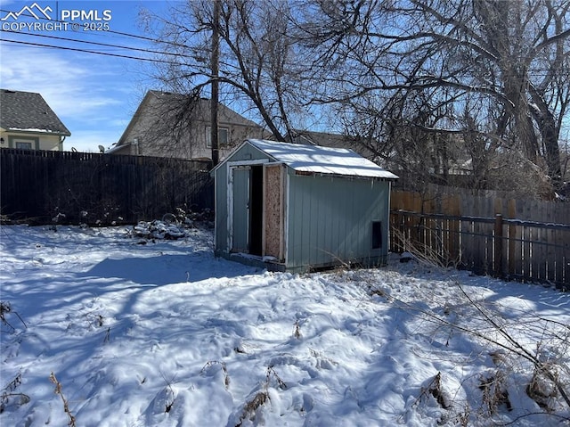 snow covered structure featuring an outbuilding, a fenced backyard, and a storage shed