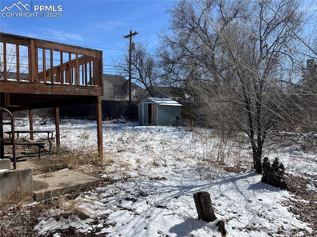 snowy yard featuring a shed, a deck, and an outbuilding