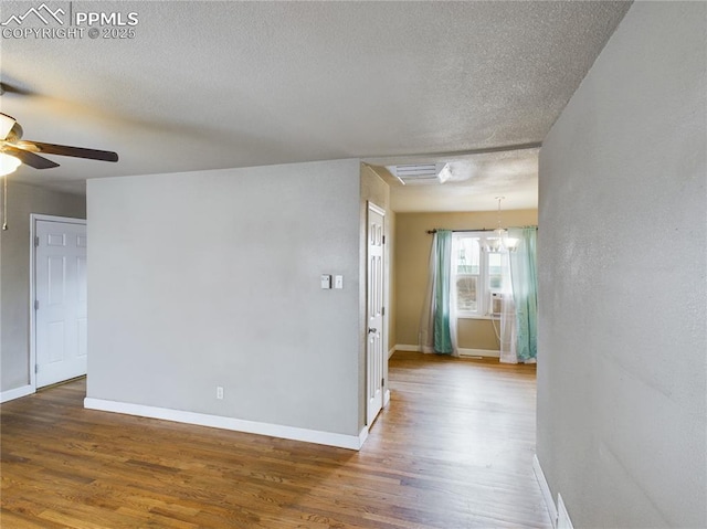 empty room featuring a textured ceiling, baseboards, wood finished floors, and ceiling fan with notable chandelier