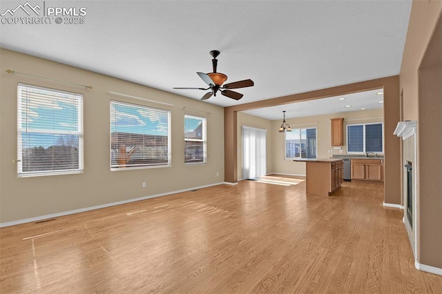 unfurnished living room with a fireplace, visible vents, a ceiling fan, baseboards, and light wood finished floors