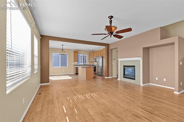 unfurnished living room featuring baseboards, ceiling fan, light wood-type flooring, a fireplace, and a sink