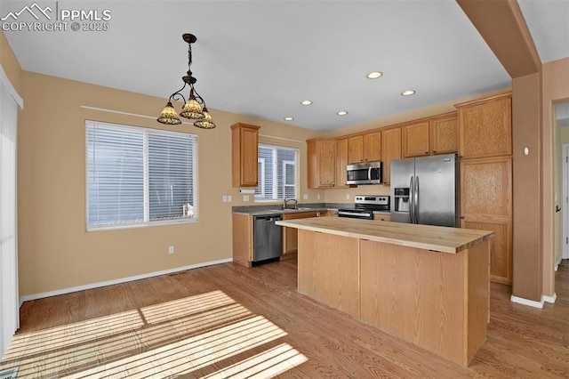 kitchen with appliances with stainless steel finishes, wood finished floors, a center island, wooden counters, and a sink