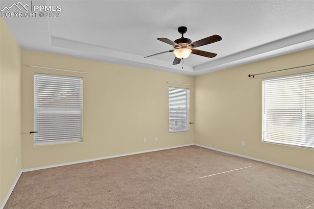 carpeted empty room featuring ceiling fan, a raised ceiling, and baseboards