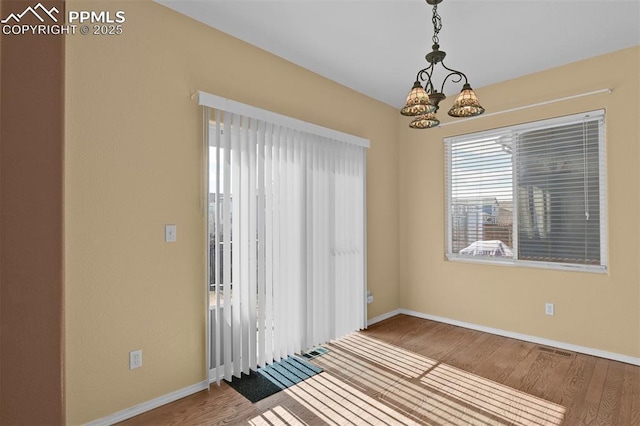 unfurnished room with an inviting chandelier, visible vents, baseboards, and wood finished floors